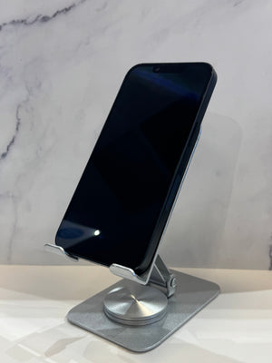 A silver metal phone stand holding a black smartphone, set against a light gray marble-patterned background.