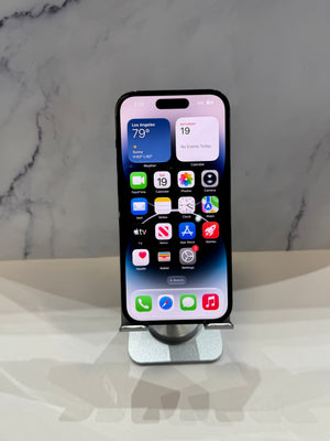 A black iPhone with its home screen visible, standing upright on a silver metal display stand against a light gray marble-patterned background.