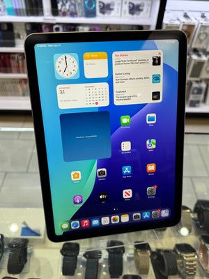 A black tablet device displaying a colorful home screen, photographed upright on a glass display counter in a retail store with watches and electronics in the background.