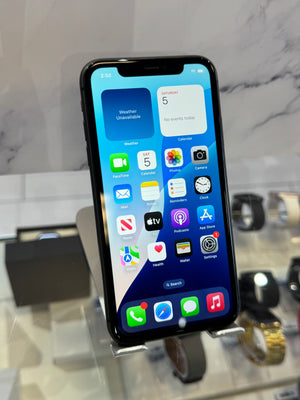 A black iPhone with its screen turned on, displaying the home screen, standing on a display stand in a watch and phone store.