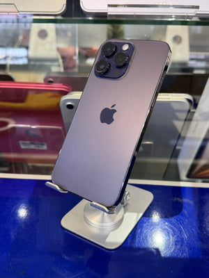 An Apple iPhone 12 Pro in purple-gray color, shown from the back on a silver display stand inside a retail store.