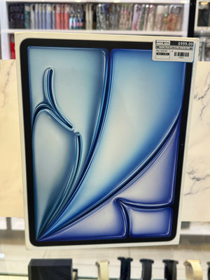 The product packing for an iPad displaying blue and light blue curved shapes, displayed on a marble-patterned stand in a retail setting. A small price sticker is visible in the top right corner.