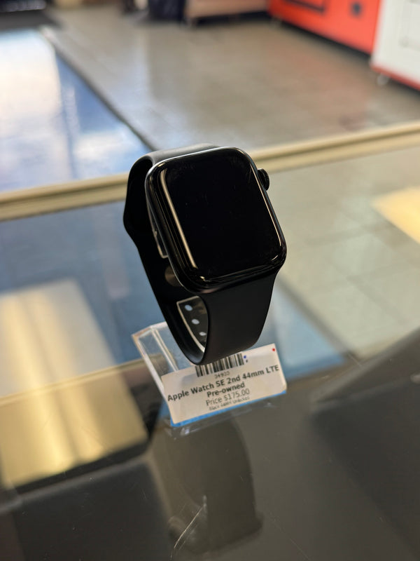 A black Apple Watch with a black sport band, resting on a glass display counter with a product tag attached.