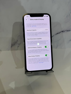 A black smartphone displayed on a small stand, showing the battery health and charging settings screen on a light gray marble-like surface.