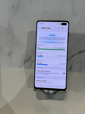 A black smartphone displayed upright on a small stand against a light marble-patterned background, showing the Google Android settings screen for Device care.