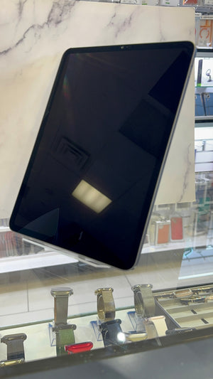 A black tablet device with a glossy screen, displayed at an angle on a stand inside what appears to be a retail store or showroom, with a marble-patterned background and watch displays below.
