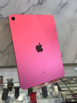 A pink Apple iPad with a glossy finish, shown from the back with the black Apple logo in the center, displayed on a stand in front of a marble-patterned wall.