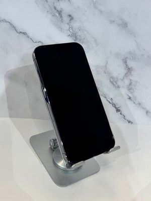 A black smartphone with a silver edge rests on a metallic silver stand against a white and gray marble-patterned background.