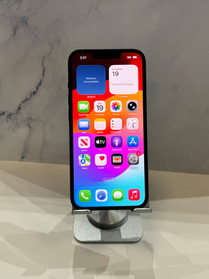 A black smartphone with a colorful home screen displayed on a silver metal stand, set against a light gray marble-patterned background.