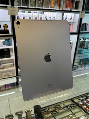 A silver Apple iPad shown from the back, resting on a glass display table inside a retail store.