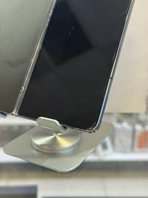 A close-up of a silver smartphone with a black screen resting on a metallic silver display stand.