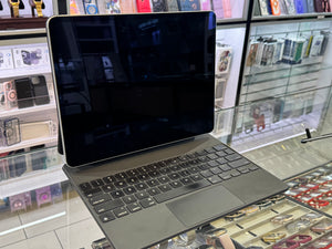 A dark gray Microsoft Surface Pro tablet with a matching keyboard cover and protective back, displayed on a glass counter inside a retail store.