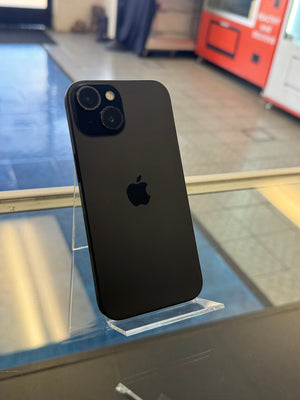 A black Apple iPhone with a dual-camera system, shown from the back and resting on a clear acrylic display stand.