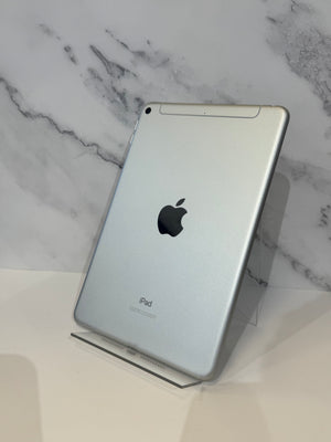 A silver Apple iPad shown from the back, standing on a clear acrylic display stand against a white marble-patterned background.