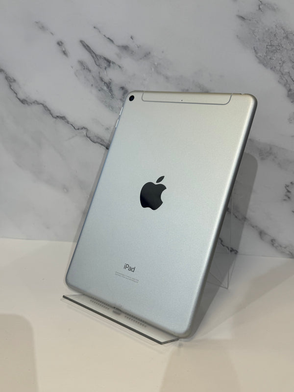 A silver Apple iPad shown from the back, standing on a clear acrylic display stand against a white marble-patterned background.