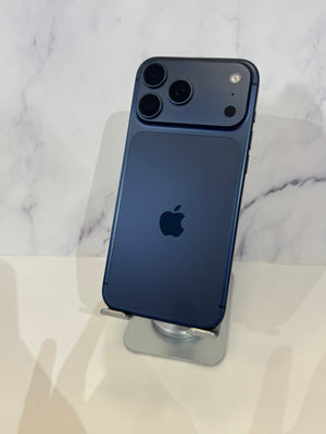 A dark blue Apple iPhone 12 Pro shown from the back, resting on a clear stand against a white marble-patterned background.