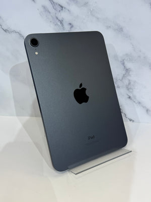 A dark gray Apple iPad shown from the back, standing upright on a clear acrylic display stand against a white marble-patterned background.