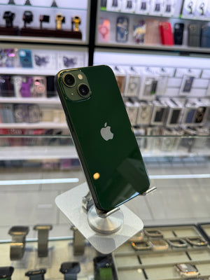 A dark green Apple iPhone with a glossy finish, shown from the back on a white display stand inside a retail store.