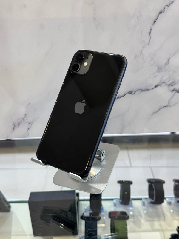 A black Apple iPhone with a glossy finish is displayed on a silver stand in a retail setting, with a marble-patterned wall in the background.