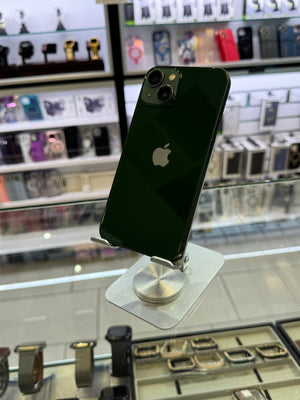 A dark green Apple iPhone 12 Pro displayed on a silver stand inside a retail store, with watch displays visible in the blurred background.