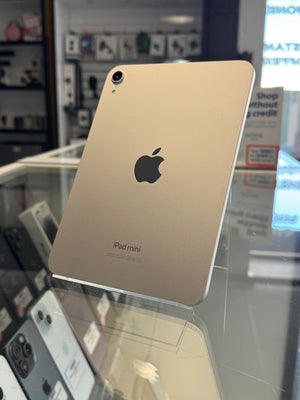A silver Apple iPad mini shown from the back, resting on a clear display stand inside a retail store.