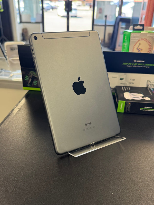 A silver Apple iPad shown from the back, resting on a dark gray surface with store display boxes in the blurred background.
