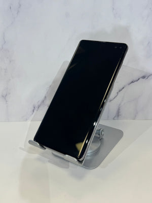 A black smartphone with a curved screen, displayed upright on a clear acrylic stand against a white marble-patterned background.