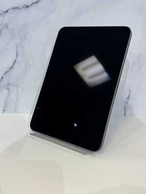 A black tablet with rounded corners displayed upright on a clear acrylic stand against a white marble-patterned background.