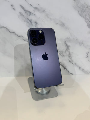 A dark blue-purple Apple iPhone 12 Pro Max standing upright on a silver metal display stand, set against a white marble-patterned background.