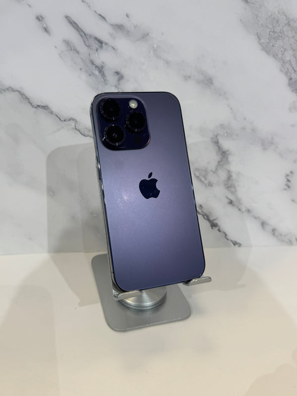 A dark blue-purple Apple iPhone 12 Pro Max standing upright on a silver metal display stand, set against a white marble-patterned background.
