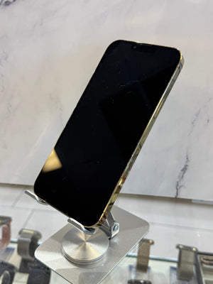 A black smartphone with a metallic gold edge, shown from a side angle mounted on a silver metal stand against a white marble-patterned background.