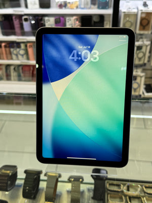 A tablet with a black bezel displaying a blue and green lock screen wallpaper, photographed inside a retail store with shelves of accessories visible in the background.