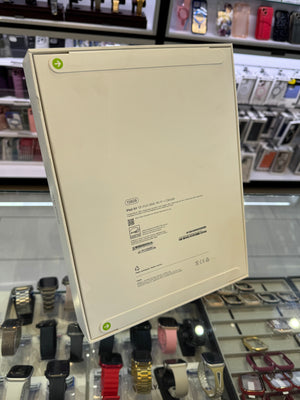 A cream-colored Apple product box, shown from the back, leaning against a glass display case filled with various smartwatches in a retail store setting.