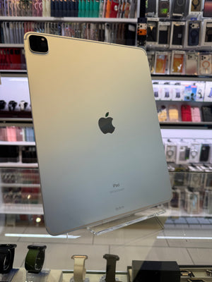 A silver-colored iPad Pro shown from the back, resting on a clear acrylic display stand inside a retail store with shelves of accessories in the background.