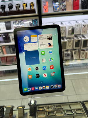 A tablet device with a black bezel and colorful home screen interface, photographed inside a retail display case with shelves of other gadgets in the background.
