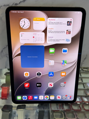 An iPad with a black bezel displaying its home screen, resting on a clear display stand.