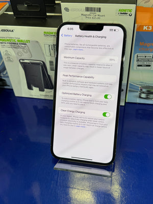 Smartphone displaying battery health and charging settings on a blue surface with electronic products in the background.