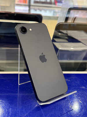 A black Apple iPhone shown from the back, resting on a clear acrylic display stand on a blue surface.