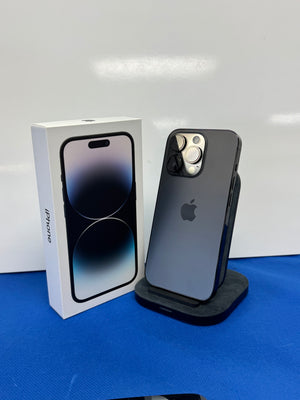 A dark gray Apple iPhone 14 Pro displayed upright on a black stand next to its original white retail box, set against a white background and a blue surface.