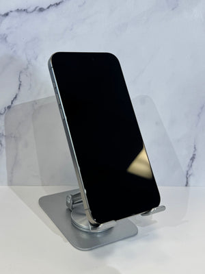 A silver smartphone with a black screen stands upright on a metallic stand against a white marble-patterned background.