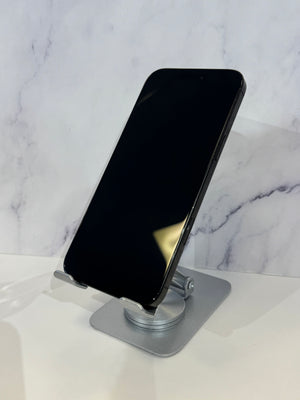 A black smartphone displayed at an angle on a silver metal stand against a white marble-patterned background.