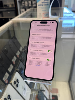 A smartphone displayed upright on a clear stand inside a retail store, showing a battery health and charging settings screen on its display.