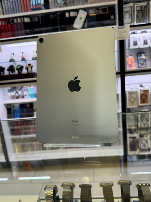 A silver Apple iPad shown from the back, photographed inside a retail store through a glass display case with reflections and store fixtures visible in the background.
