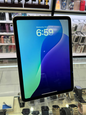 A tablet with a black bezel displaying a blue and green lock screen wallpaper, standing on a clear display stand inside a retail store with shelves of accessories in the background.