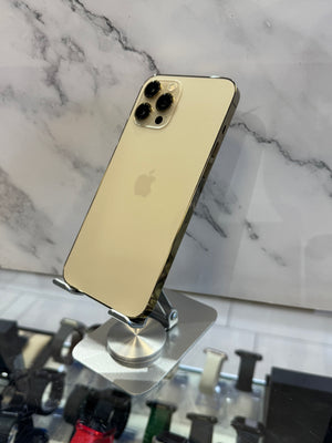 A gold-colored Apple iPhone Pro shown from the back, resting on a silver metal display stand against a white and gray marble-patterned background.