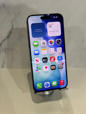 A black iPhone with its screen on, resting on a silver metal display stand against a light gray marble-patterned background.