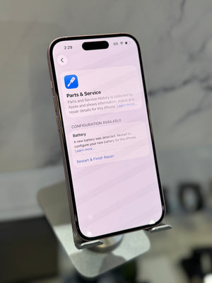 A close-up of an iPhone displaying the Apple Parts & Service app on its screen, resting on a metallic stand in a blurred indoor setting.