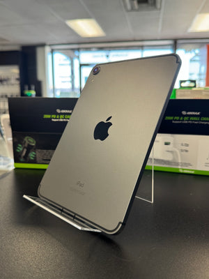 A silver Apple iPad shown from the back, resting on a clear acrylic display stand on a dark countertop inside a store.