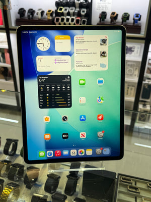 A large iPad with a black bezel displaying the iOS home screen, set on a clear display stand inside a retail store with watch displays in the background.