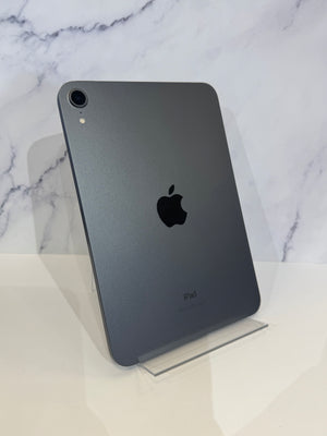 A dark gray Apple iPad shown from the back, standing upright on a clear acrylic display stand against a white marble-patterned background.